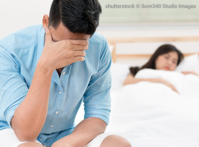 Mann unglücklich und enttäuscht über die erektile Dysfunktion, während seine Frau schlafend im Bett liegt