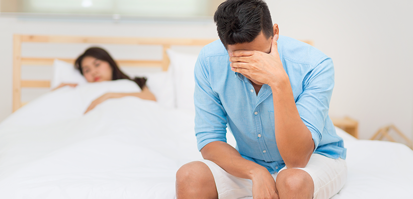 Mann unglücklich und enttäuscht über die erektile Dysfunktion, während seine Frau schlafend im Bett liegt 